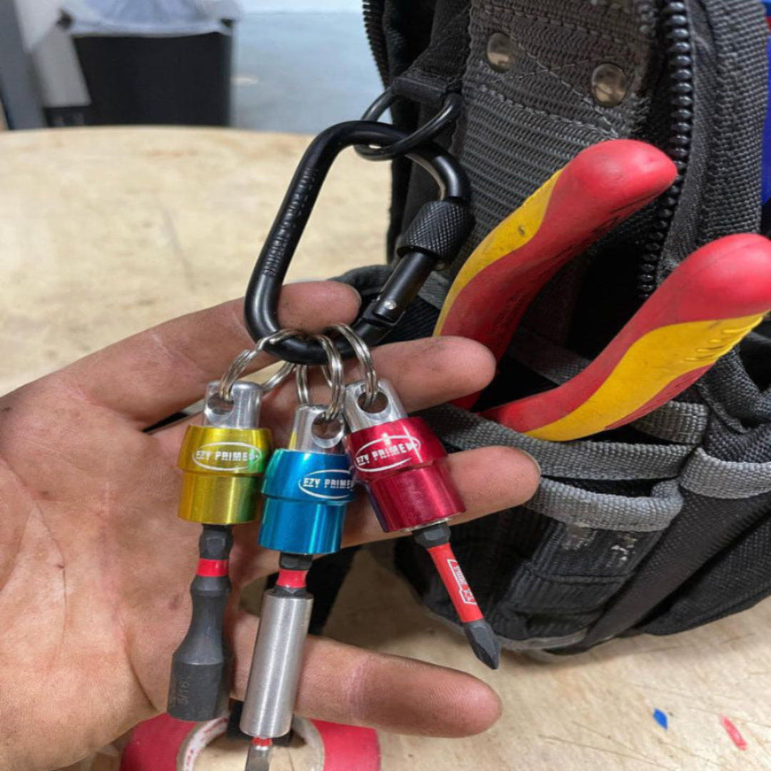 Set of colorful pullback bit holders held by a hand, with a tool belt in the background.
